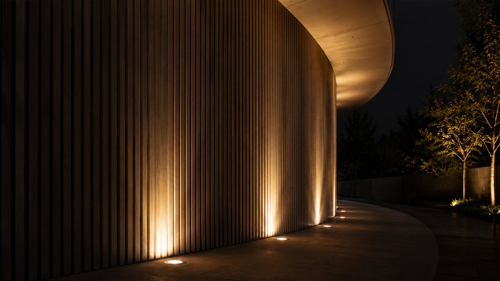 Uplighting along a curved, vertically ribbed facade beside a pathway at night
